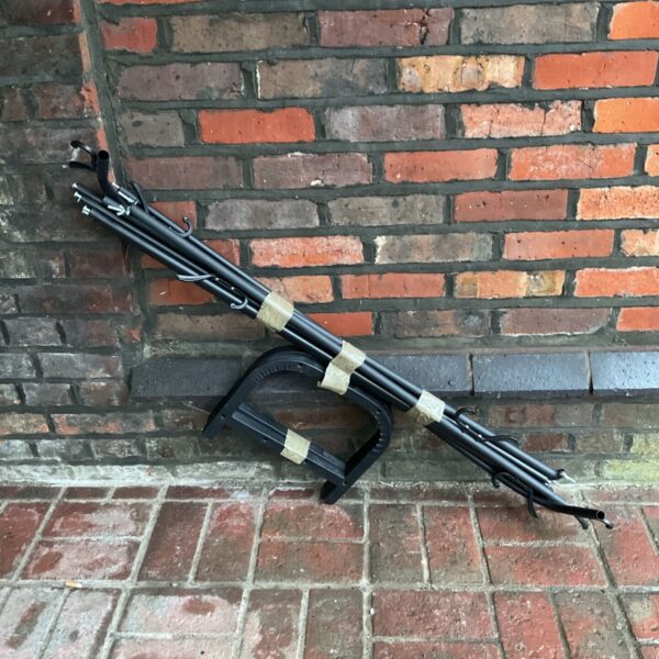 Black collapsible clothes rail with hooks, bundled with tape on pavement