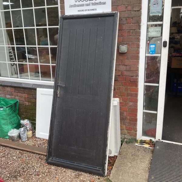 Black composite door leaning against brick wall.