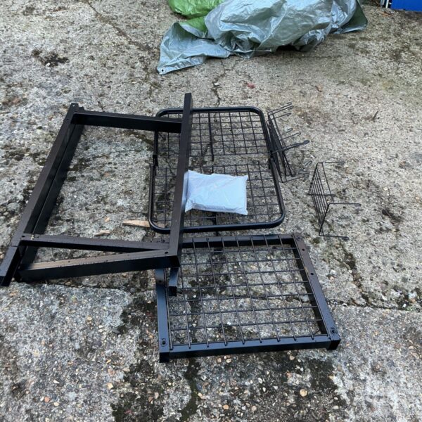 Disassembled black metal storage shelf unit components with wire mesh trays laid out
