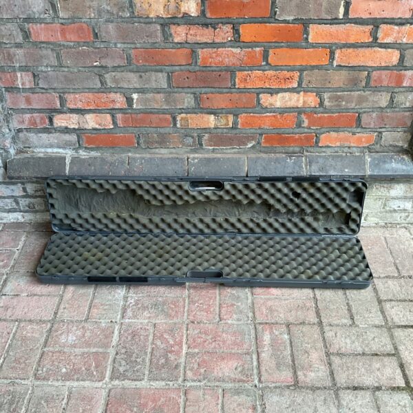 Black rifle case leaning against a brick wall.