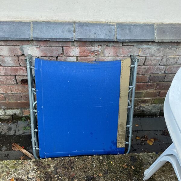 Blue fabric folding sun lounger with grey metal frame against brick wall