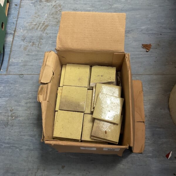 Open cardboard box filled with pale yellow-cream glazed ceramic tiles