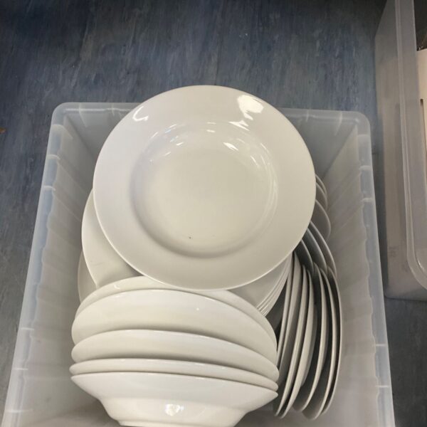 Box of white porcelain bowls and plates in a clear plastic crate