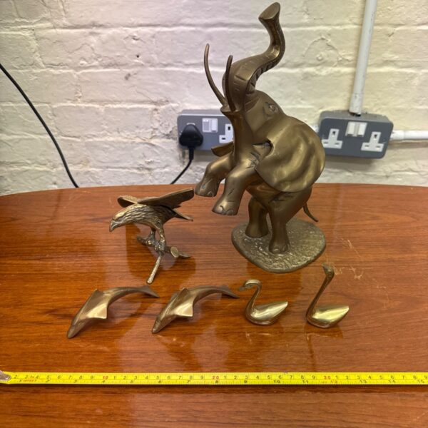 Brass elephant, eagle, pair of dolphins and pair of swans on a wooden table