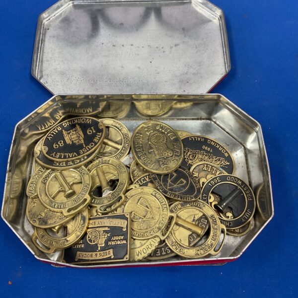 Selection of brass steam rally plates displayed in a silver octagonal tin