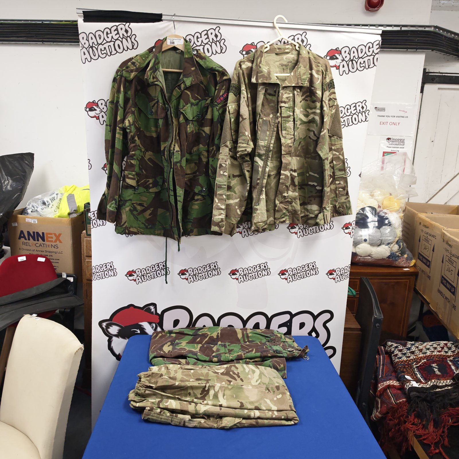 Two British forest camouflage military jackets and folded trousers displayed on a stand