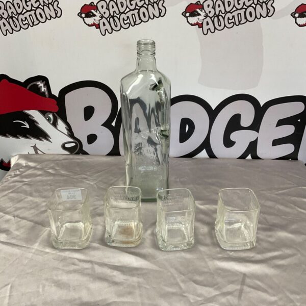 Clear glass bottle and four Bushmills whisky tumblers on grey fabric