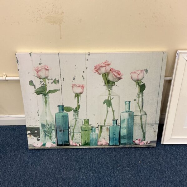 Canvas wall art of pink roses in glass bottles on a white wooden backdrop