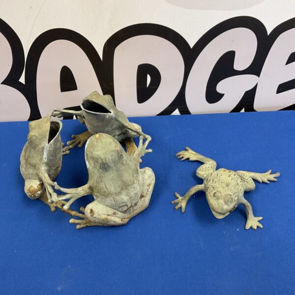 Three weathered cast metal dancing frogs and a toad on blue surface
