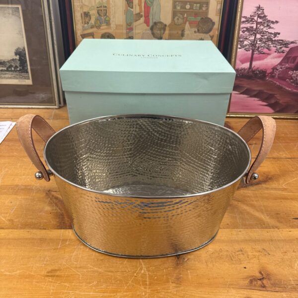Hammered metal champagne bucket with leather handles, a stylish serving piece.