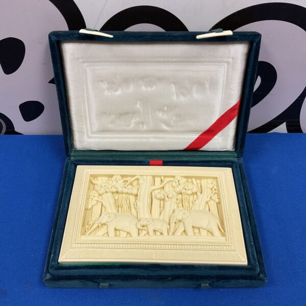 Cream carved resin panel of elephants in a jungle procession, displayed in green velvet case