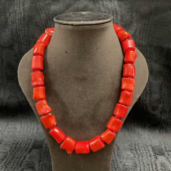 Chunky red coral bead necklace with polished barrel-shaped beads on display stand