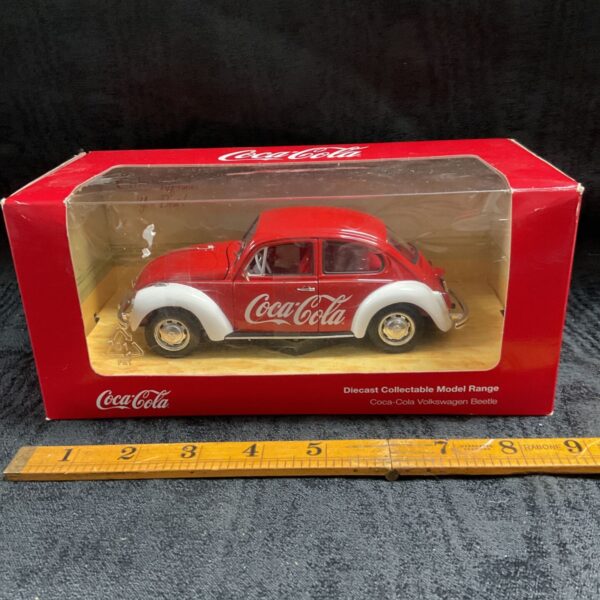 Boxed red and white Coca-Cola Volkswagen Beetle diecast model in display window