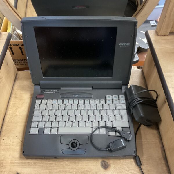 Compaq Contura laptop with WiFi dongle and charger on wooden surface