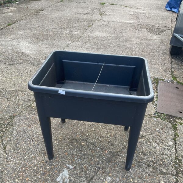 Dark plastic compost holder with legs in a garden setting.