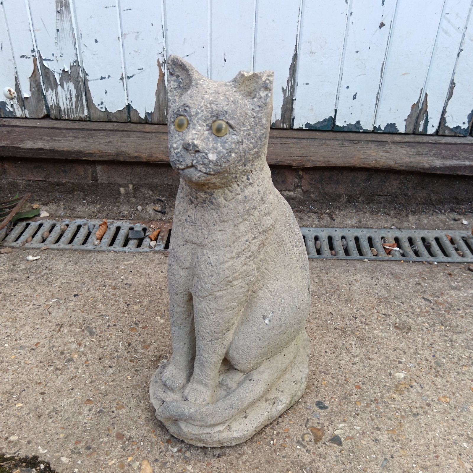 Vintage concrete garden cat statue in a weathered garden setting.