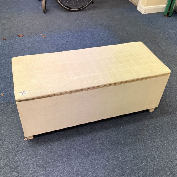 Cream upholstered storage ottoman with grid-patterned padded lid on blue carpet