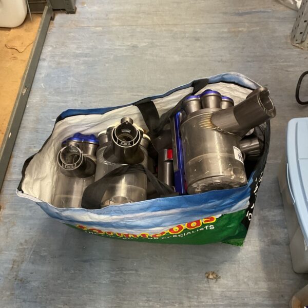 Disassembled Dyson cordless vacuum bodies in a woven carrier bag