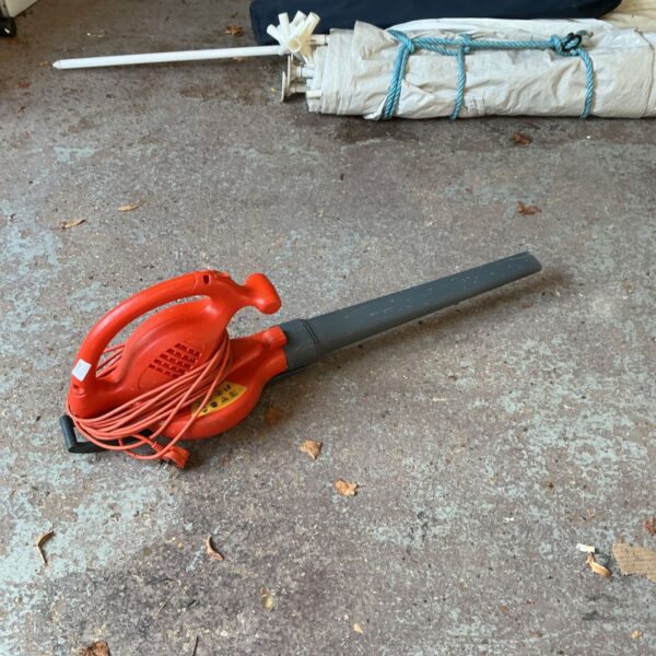 Red and grey electric leaf blower with mains cable coiled around its body