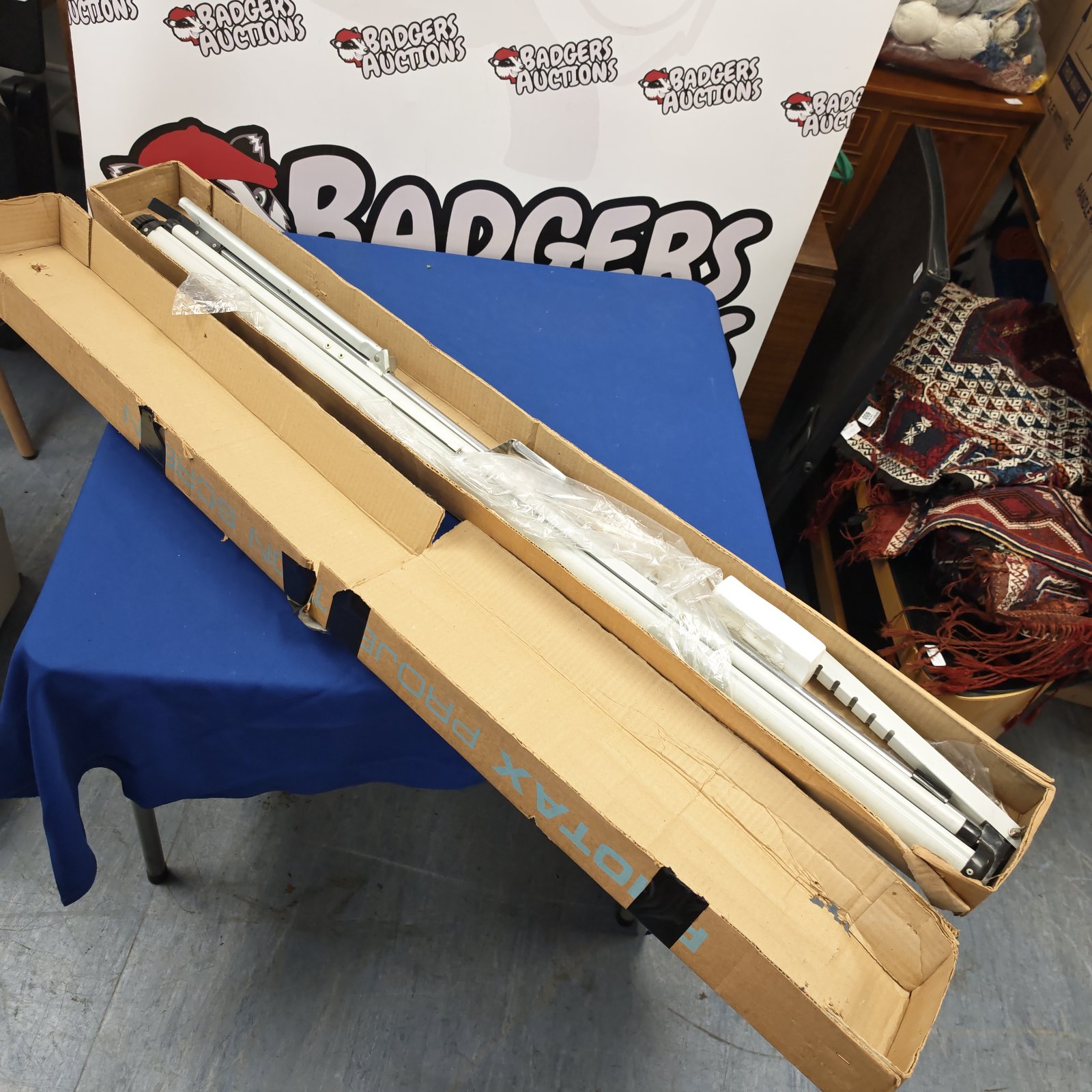 Fiotax box projector screen in cardboard packaging with white tubular supports