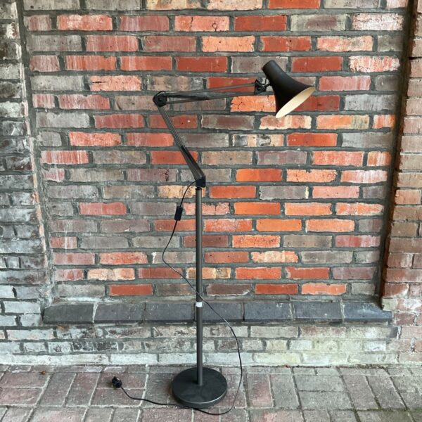 Dark brown floor standing Anglepoise style lamp with articulated arm against brick wall