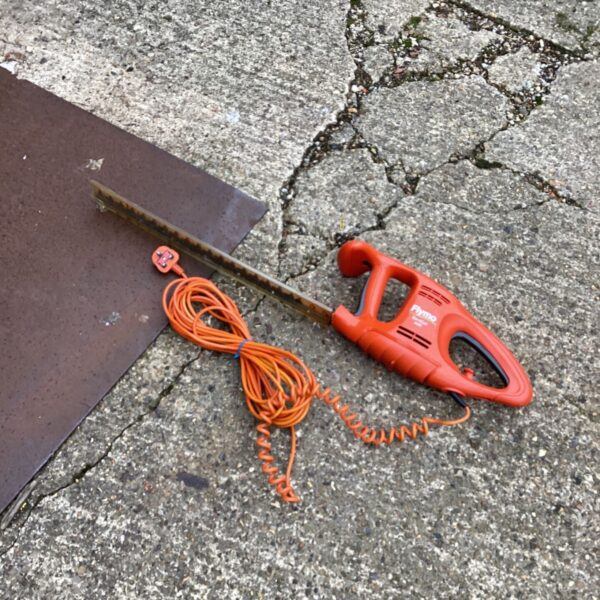 Orange Flymo electric hedge trimmer with coiled cable on concrete ground