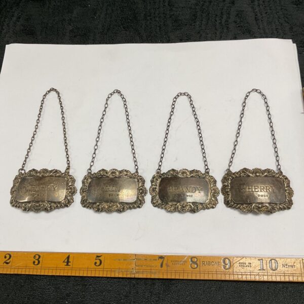 Four hallmarked silver bottle labels engraved Whisky, Gin, Brandy and Sherry on white paper