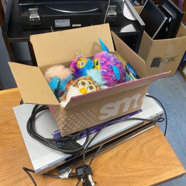 Box of Furby interactive toys with two silver DVD players and cables
