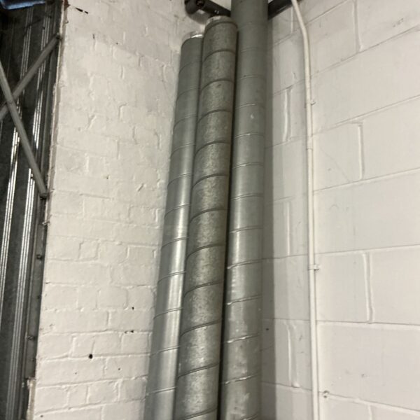 Five galvanised metal spiral ducting pipes mounted against a white painted brick wall