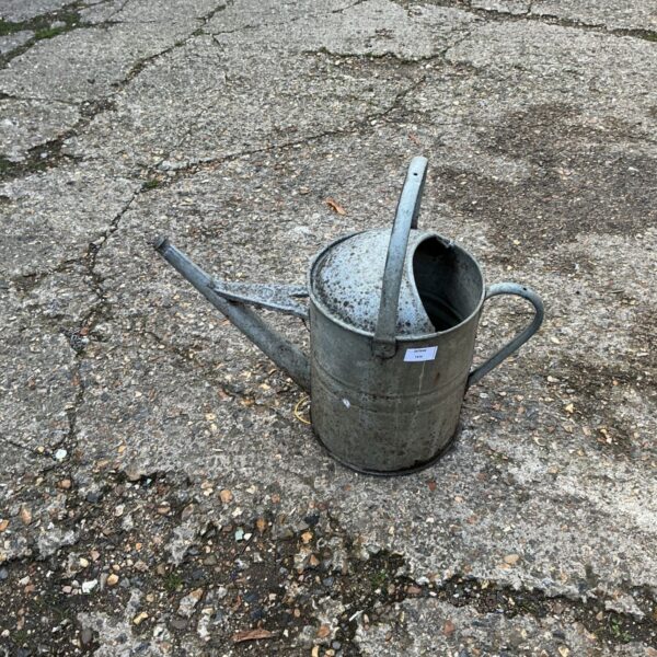 Grey galvanised watering can with long spout and side handle on paving