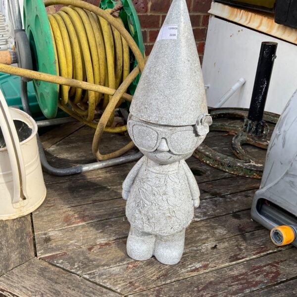 Weathered grey garden gnome figurine with sunglasses in a garden setting.