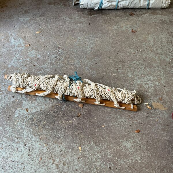 Cream knotted rope garden hammock gathered around a wooden spreader bar