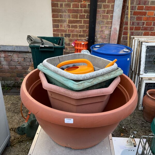Assorted plastic garden planters and a watering can in a garden setting.