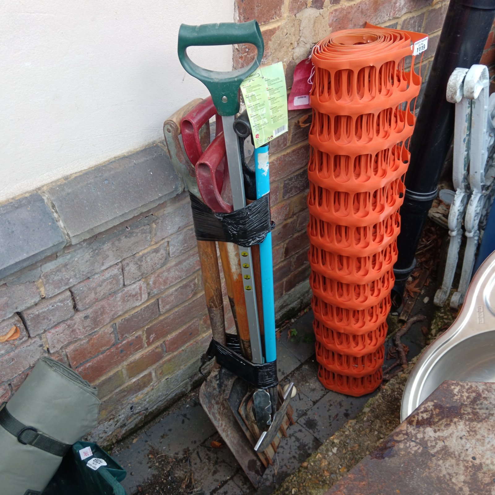 Bundle of used gardening tools including a spade and plant support.