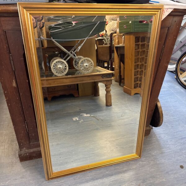 Ornate gilt framed mirror reflecting a cluttered room.