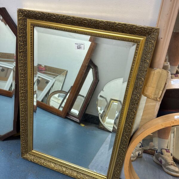 Ornate gilt framed mirror with bevelled glass reflecting a room.