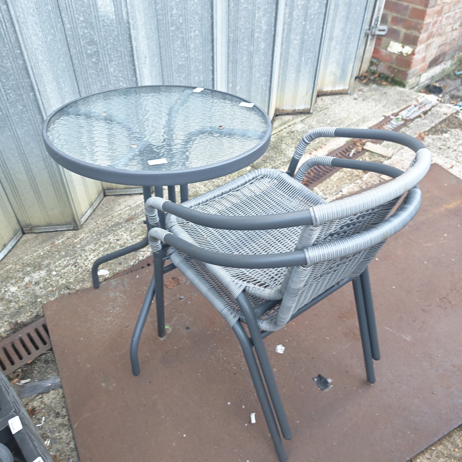 Round glass top garden table with two grey woven metal frame chairs