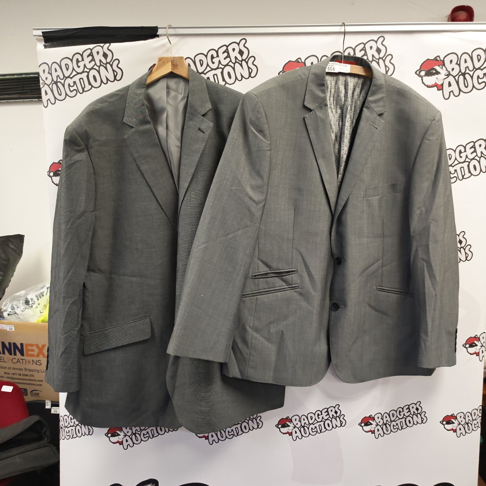 Two grey two-button suit jackets hanging on a display backdrop
