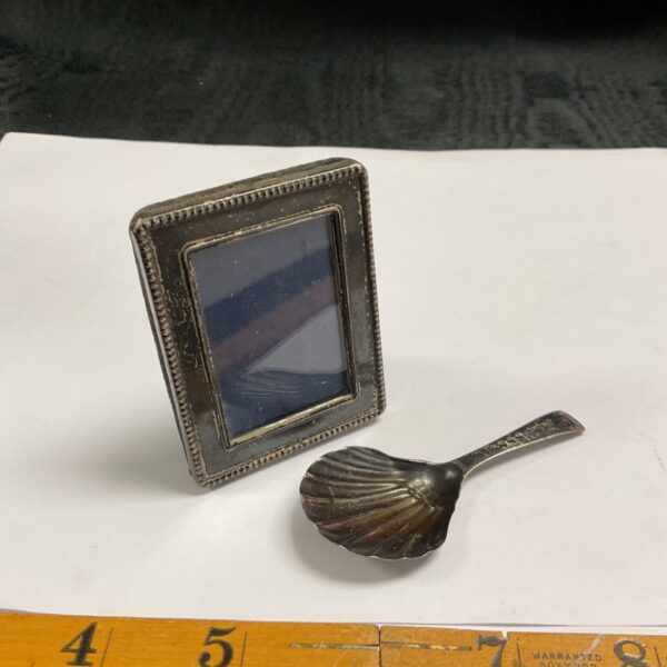 Small Victorian silver picture frame beside a Georgian silver shell caddy spoon on white paper
