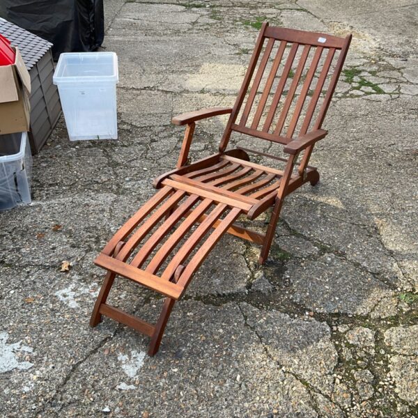 Warm-toned hardwood reclining garden chair with footrest in a garden setting.