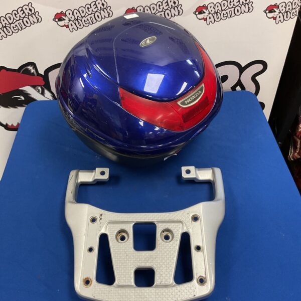 Blue Honda motorcycle top case beside silver Honda luggage rack on blue surface