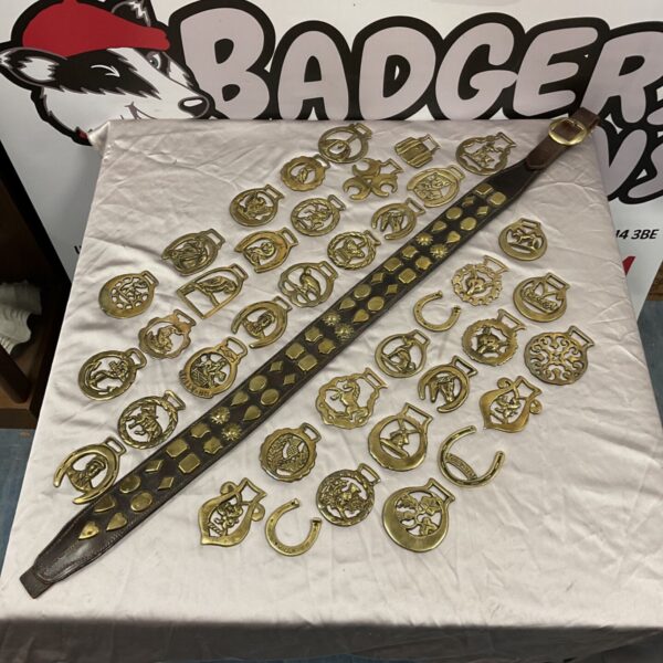 Collection of brass horse brasses and studded leather belt laid out on a table