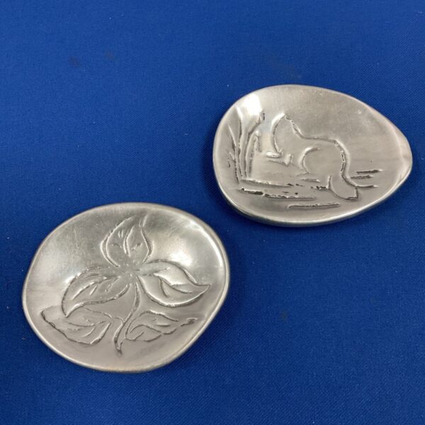 Two vintage cast aluminium trinket dishes with leaf and animal relief designs on blue background