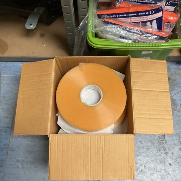 Large amber industrial machine packaging tape roll in open cardboard carton