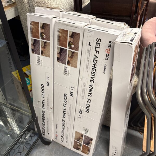 Stack of seven unopened packs of Inmozata self adhesive vinyl flooring.