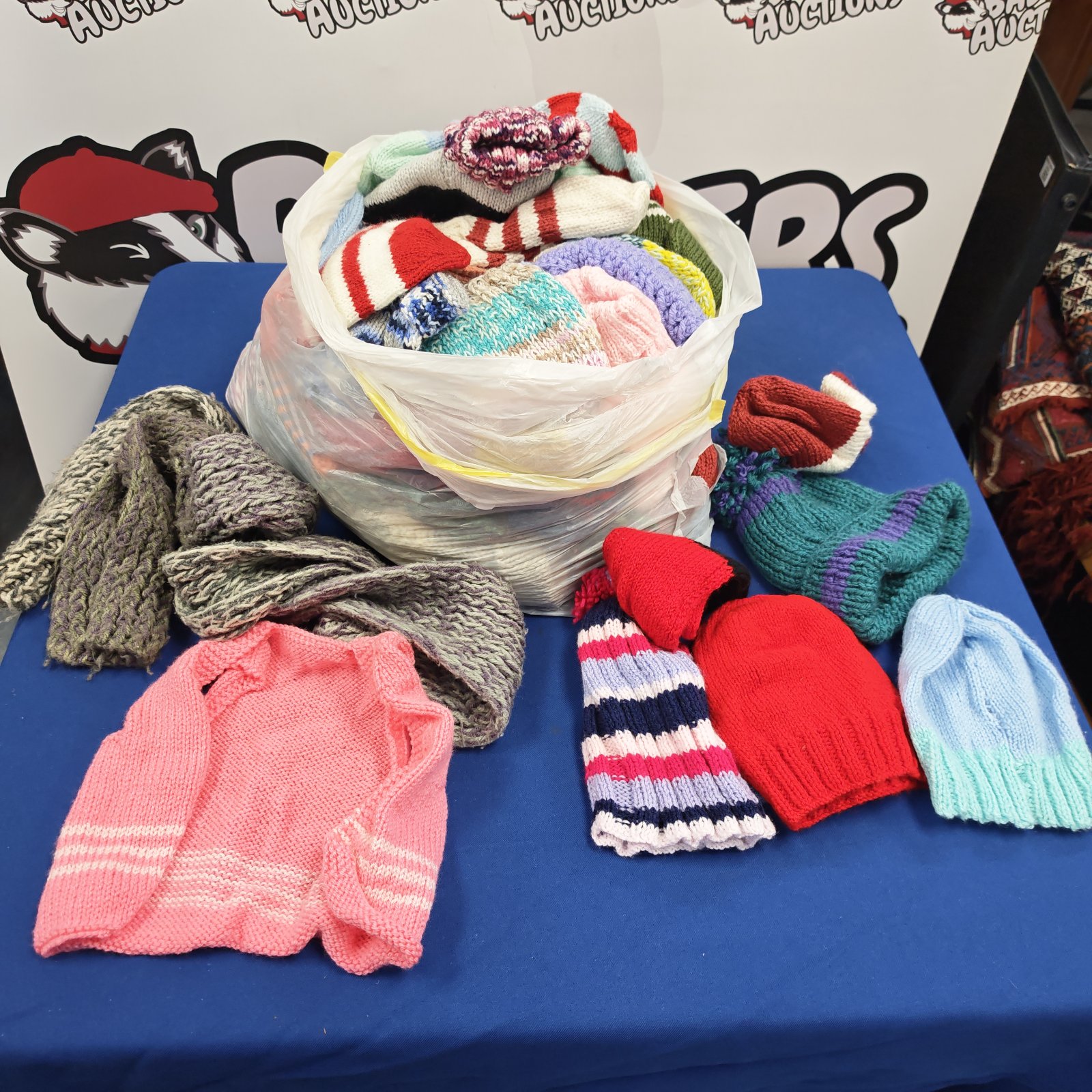 Bag of knitted woolly hats, scarves and pink cardigan on blue table