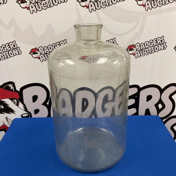 Large clear glass carboy bottle with rounded body and narrow neck on blue surface