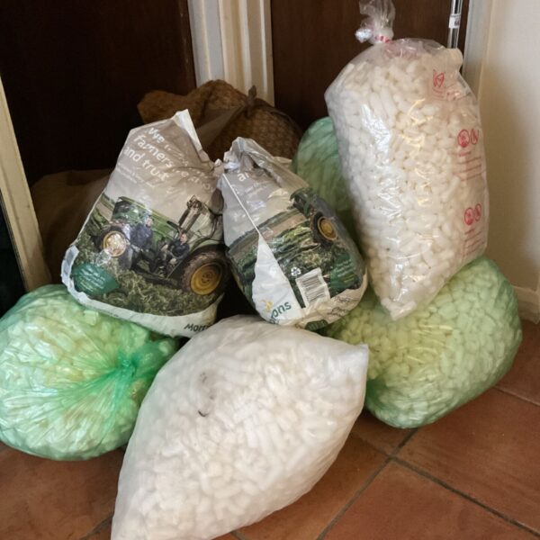 Large lot of white and green foam packing peanuts in bags on terracotta tiles