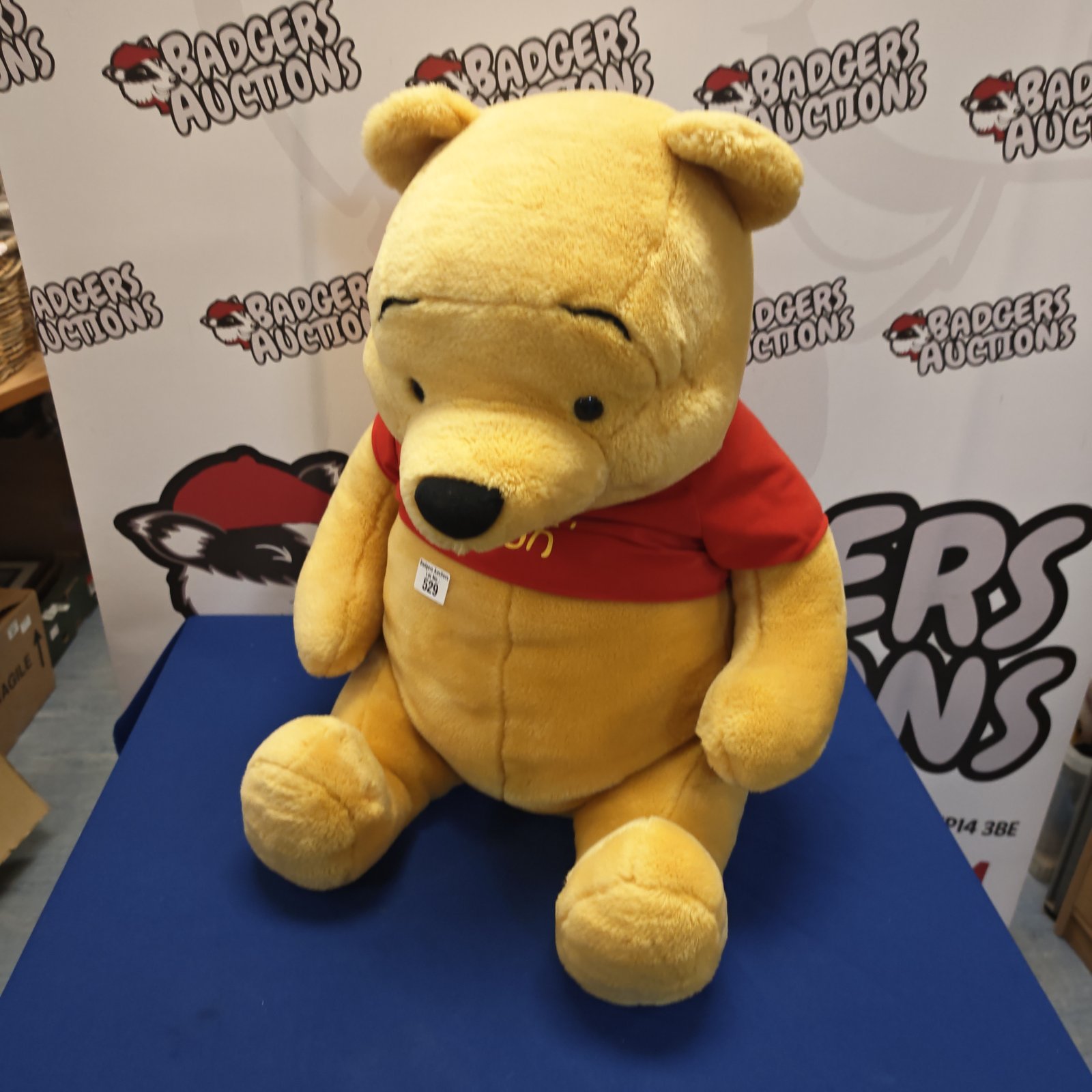 Large yellow Winnie the Pooh cuddly toy with red shirt.