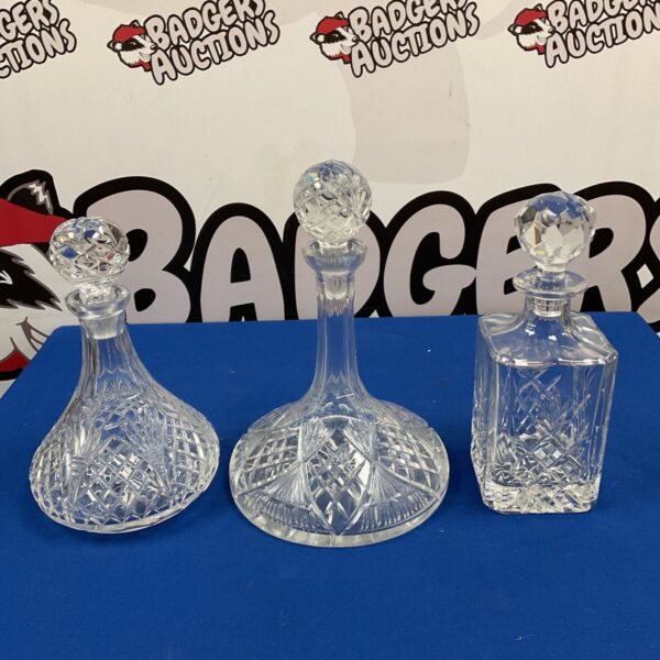 Three cut lead crystal decanters with stoppers on blue display cloth